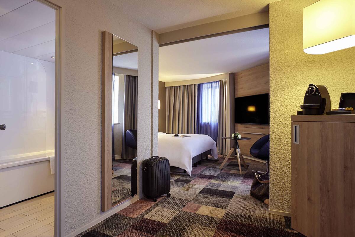 Une chambre d’hôtel avec un lit, un bureau, une chaise, une valise et un téléviseur.