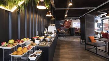 Zona de bufé con diversas frutas y platos, iluminación moderna y un área de estar con vistas.