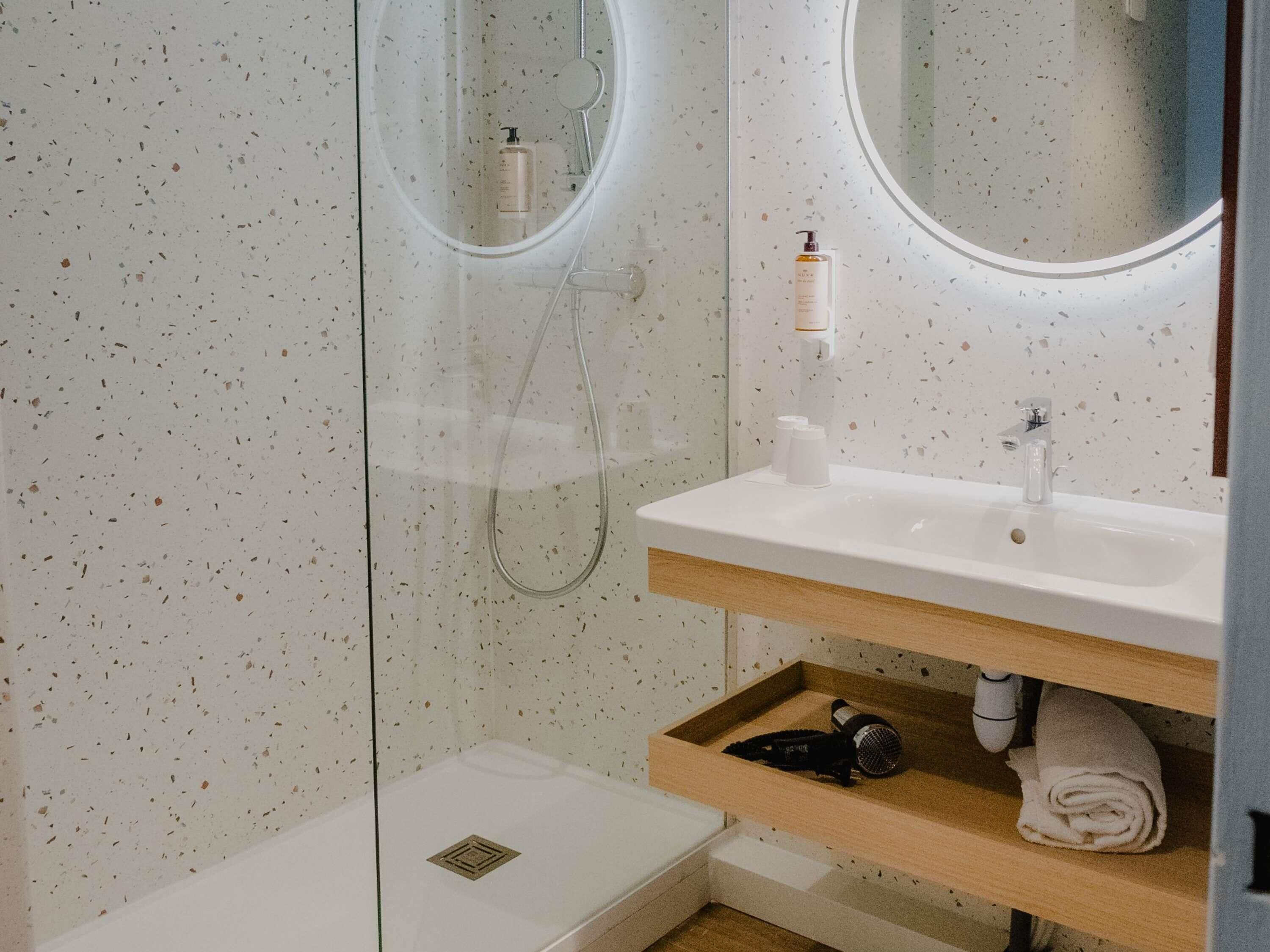 A modern bathroom with a glass shower enclosure, a white sink with a wooden countertop, and a mirror above the sink.