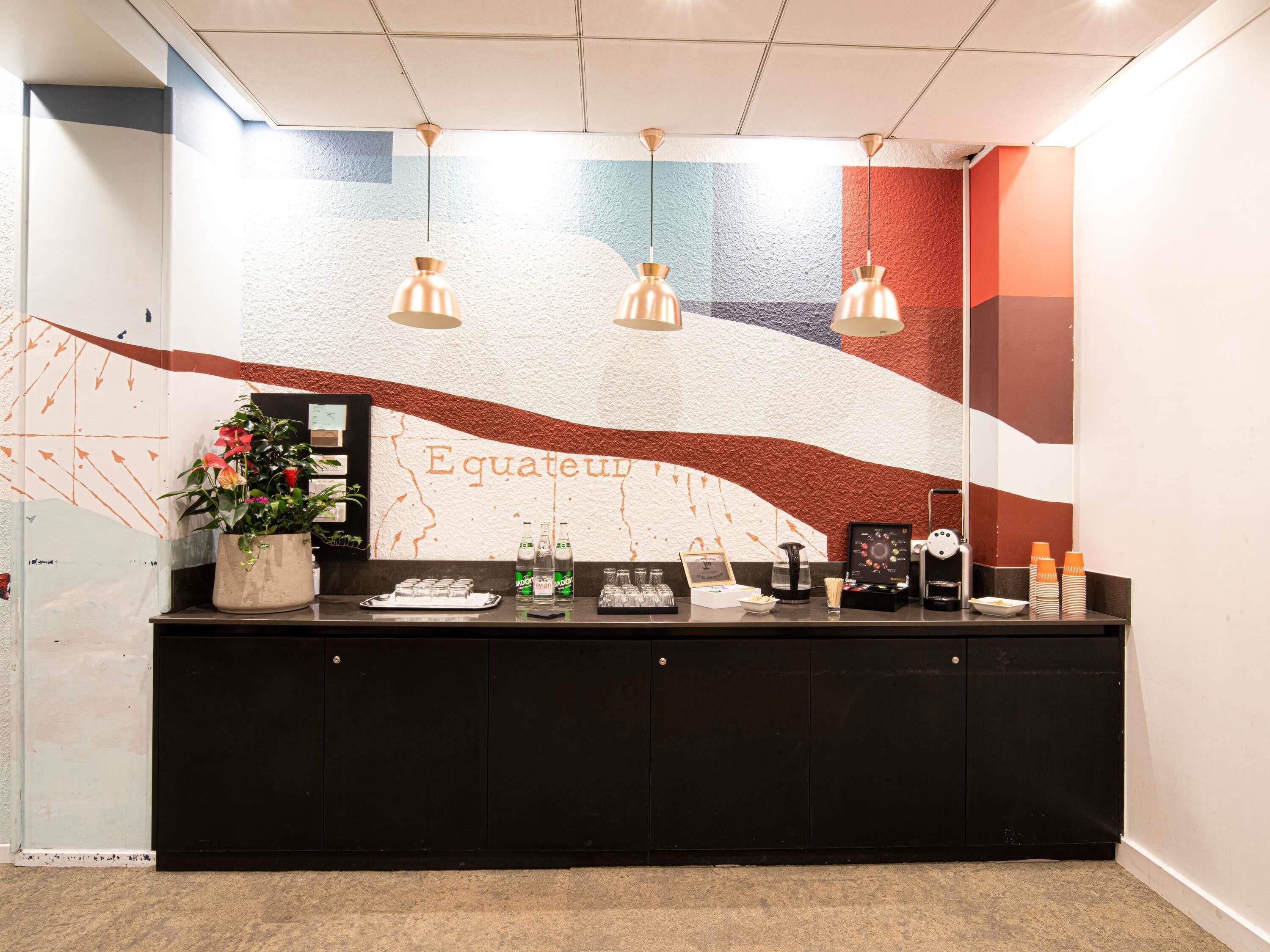A reception desk with a mural, a potted plant, and various amenities like bottles and a coffee machine.