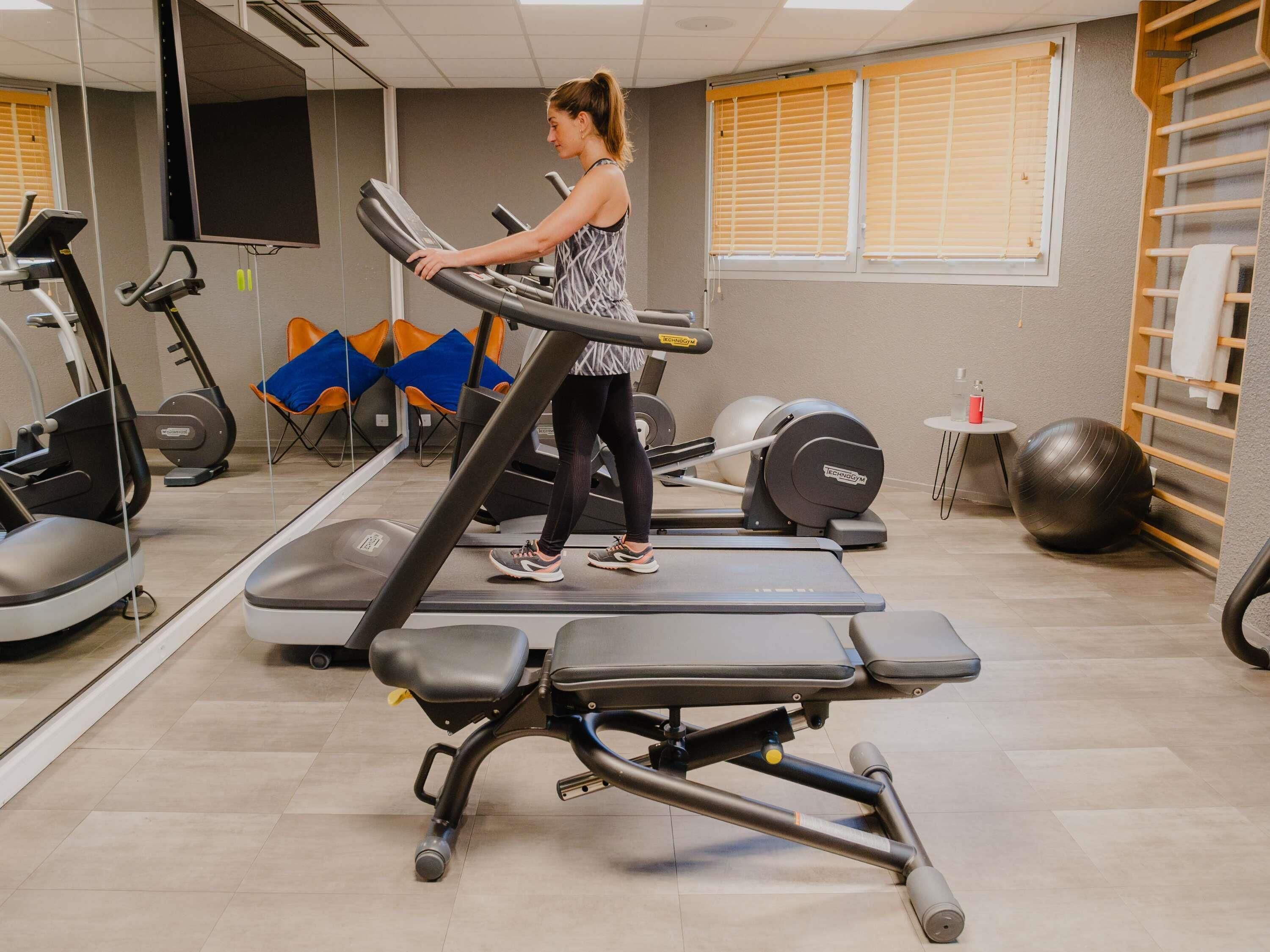 Une salle de sport équipée de tapis de course, de ballons d’exercice et de chaises.