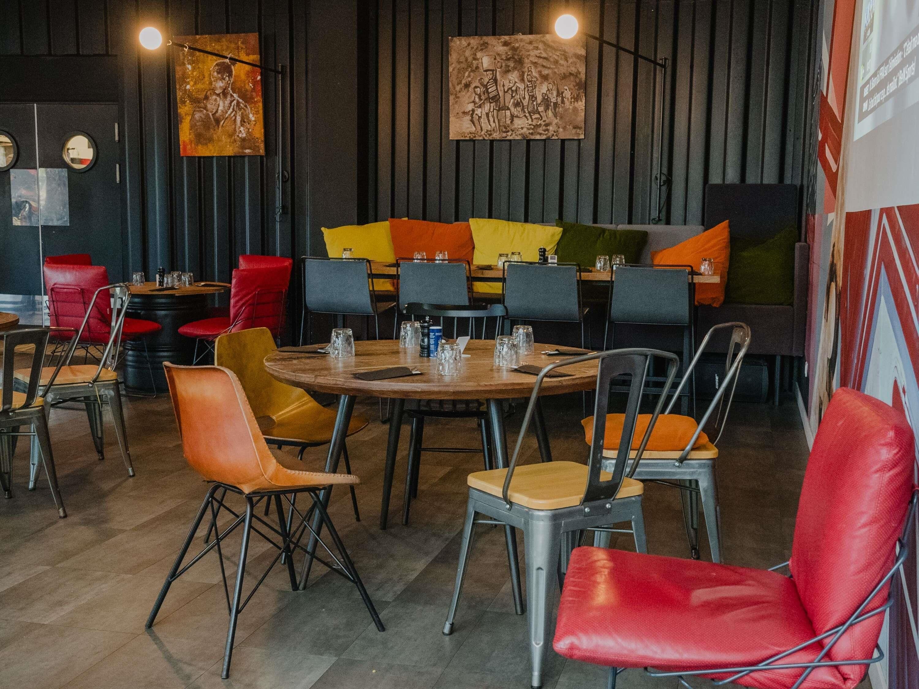 A modern restaurant with round tables, red and yellow chairs, and artwork on the walls.