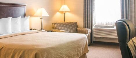 A hotel room with a large bed, two bedside lamps, a chair, an air conditioning unit, and a window with curtains.