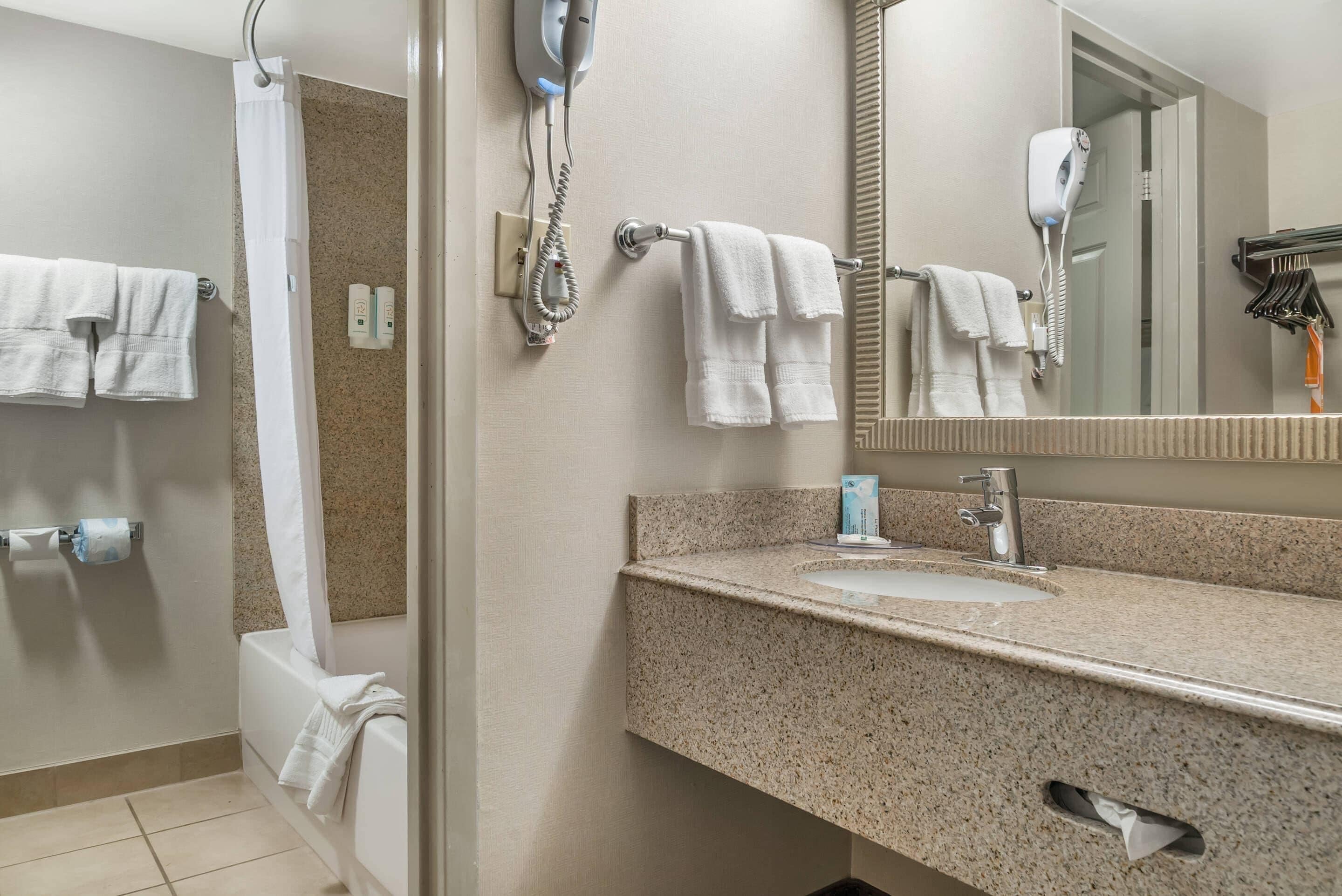 A bathroom with a granite countertop sink, a mirror, a hairdryer, and multiple towels.