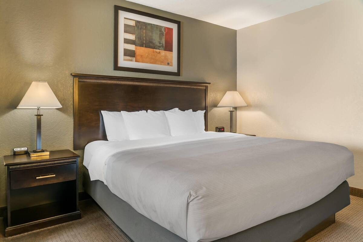 Ein ordentlich gemachtes Bett mit weißen Leinen, einem dunklen Holzkopfende und zwei Nachttischlampen.