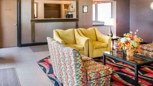 Un vestíbulo con mostrador de recepción, un sillón amarillo, sillones estampados, una mesa de centro de vidrio y un arreglo floral.