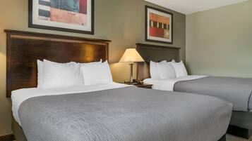 A hotel room with two beds, a wooden headboard, a lamp, and artwork on the walls.