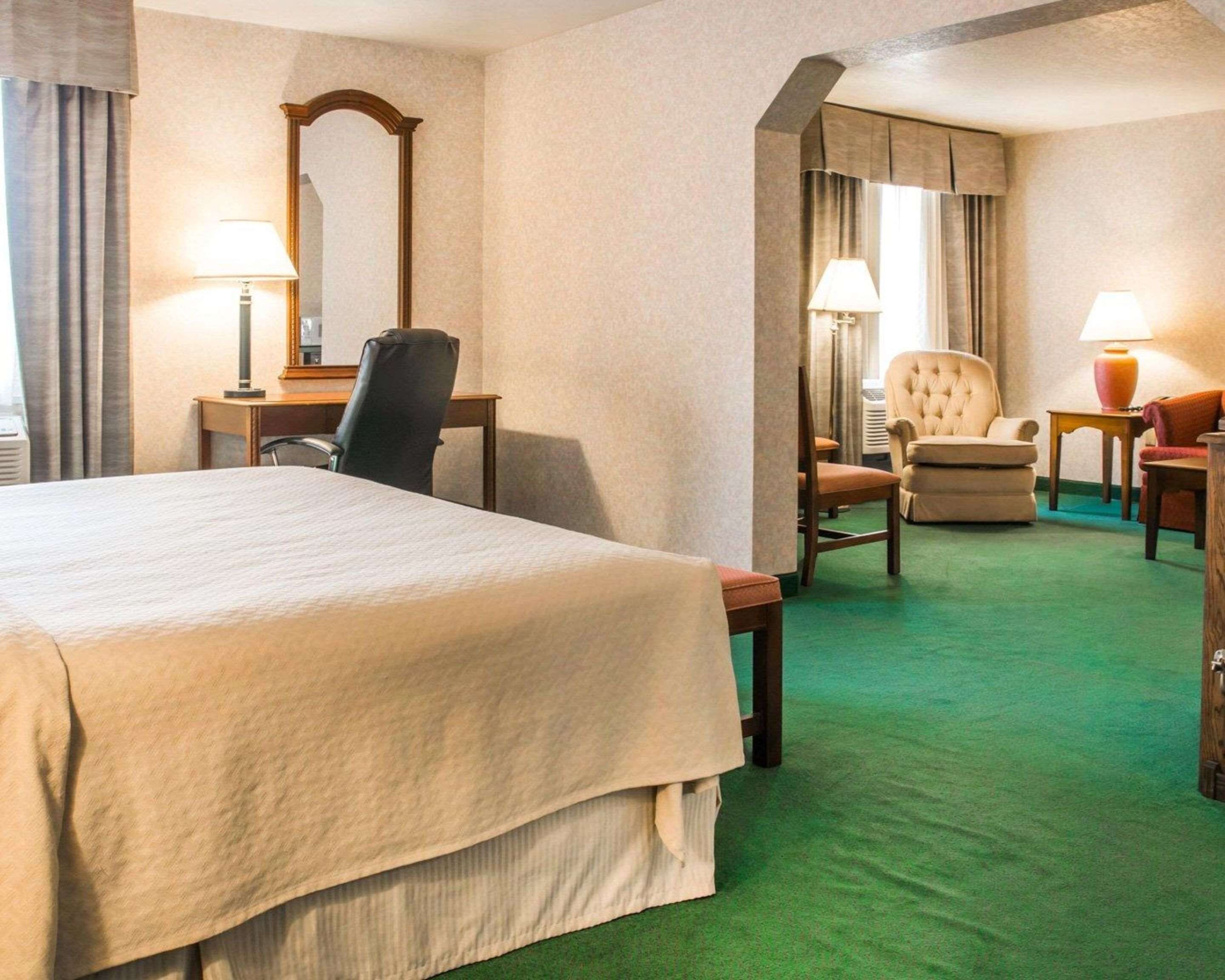 A hotel room with a large bed, a desk with a chair, a separate armchair, and a small table with a lamp.