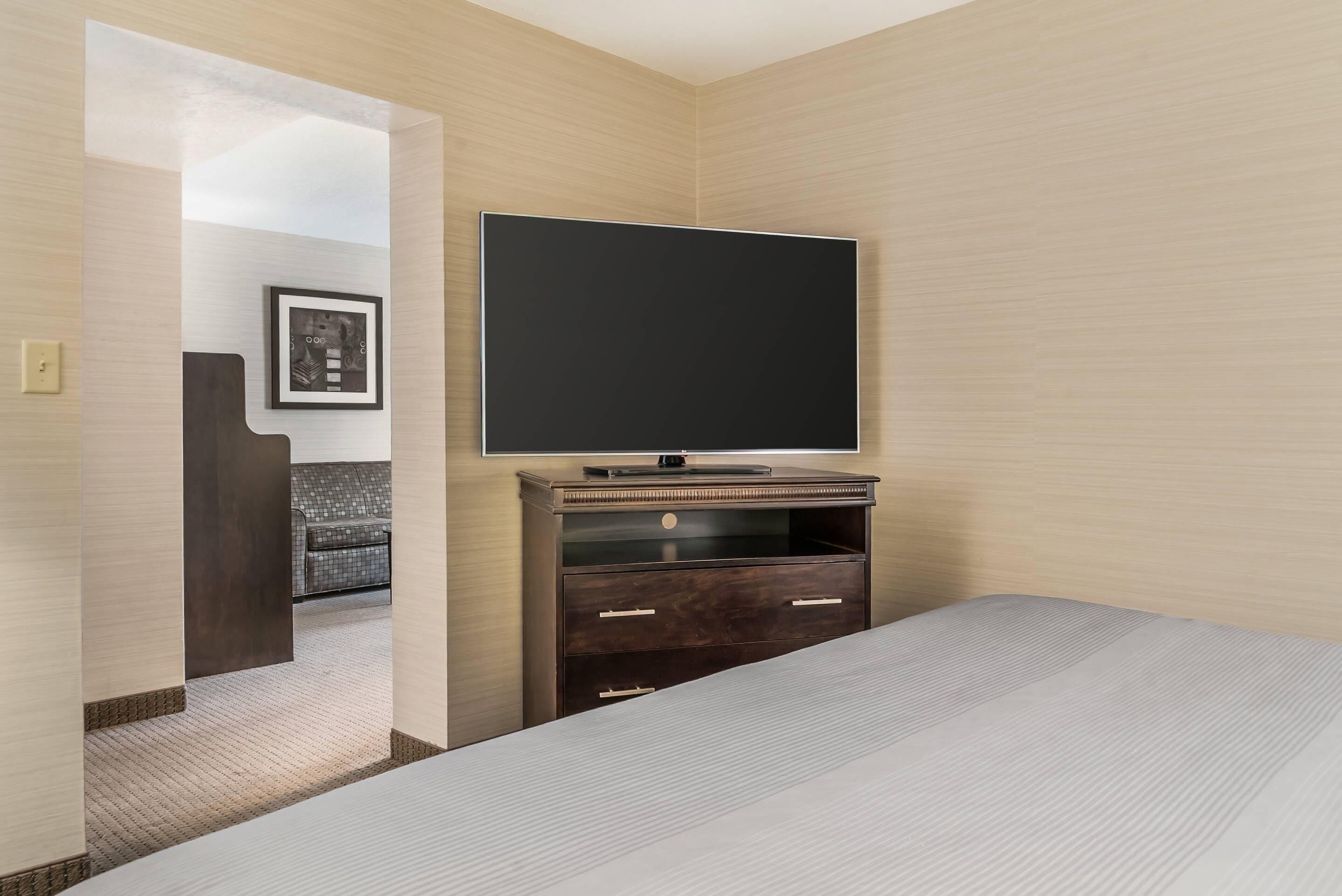 A hotel room with a bed, a TV on a wooden stand, a framed picture on the wall, and a door leading to another room.
