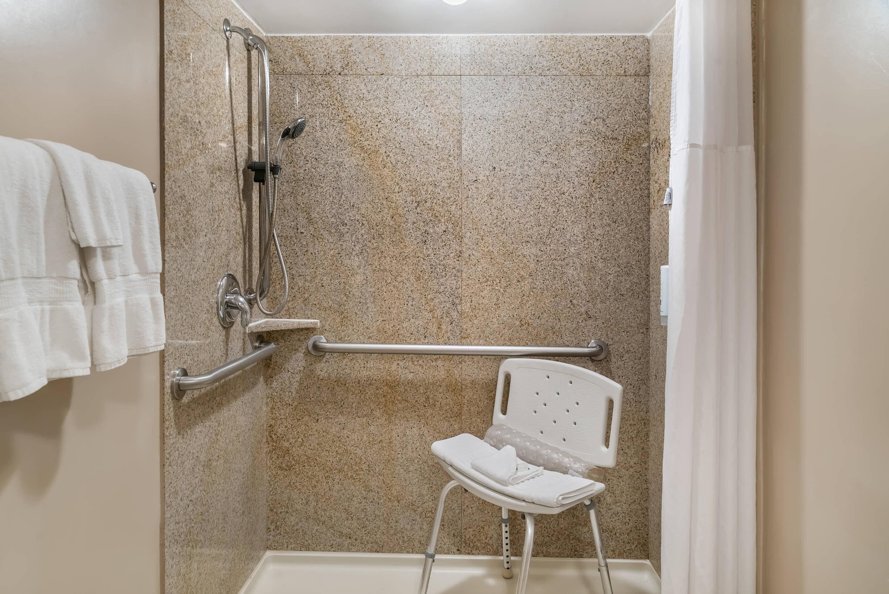A shower area with a grab bar, a white chair, and a towel rack.