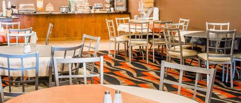 A hotel dining area with round tables, chairs, and a buffet counter.