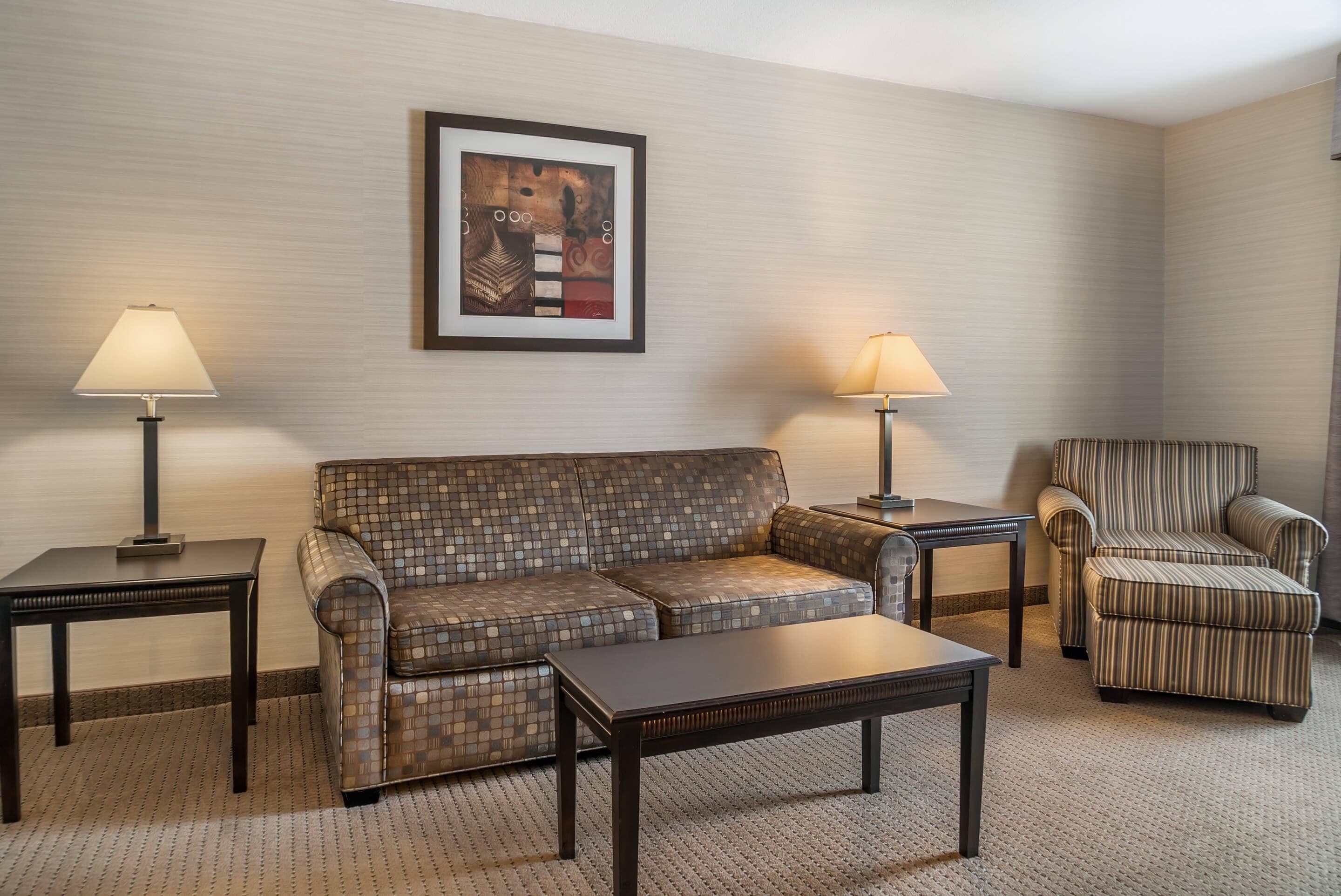 A hotel room with a patterned sofa, two armchairs, a coffee table, and two lamps.