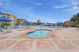 Un espace piscine agrémenté de chaises longues et de parasols, entouré d’immeubles.