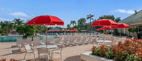 A poolside area with red umbrellas, lounge chairs, and a brick patio.