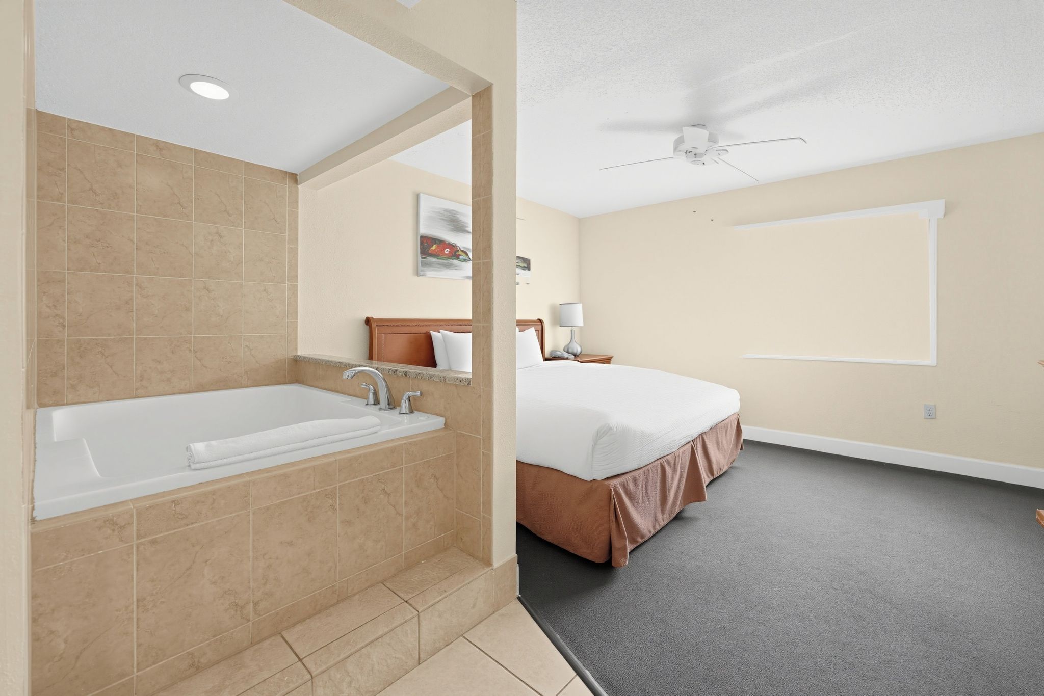 A hotel room with a large bathtub, a bed with a brown headboard, and a ceiling fan.