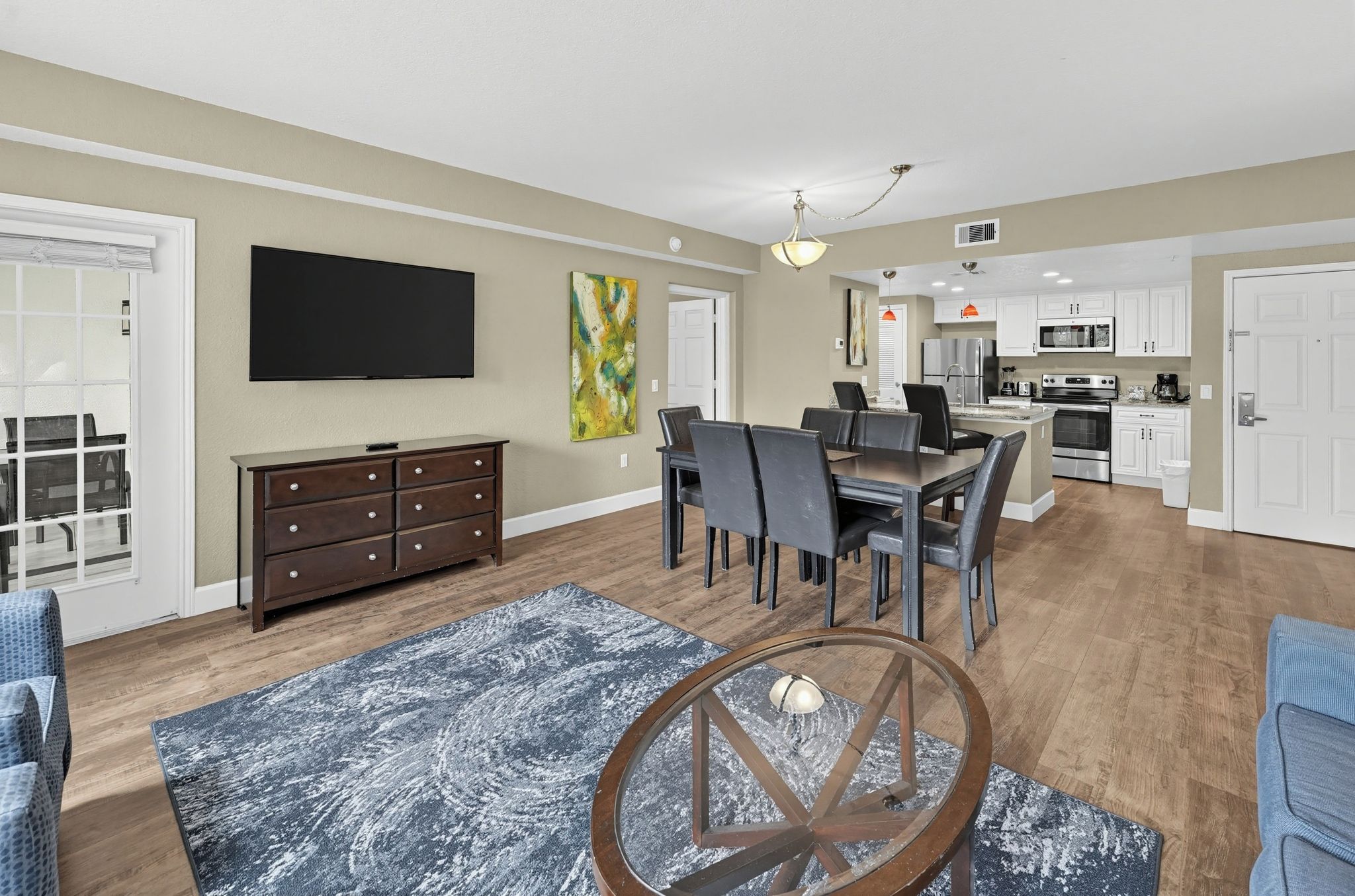 A modern living room with a dining area, kitchen, and a large flat-screen TV mounted on the wall.