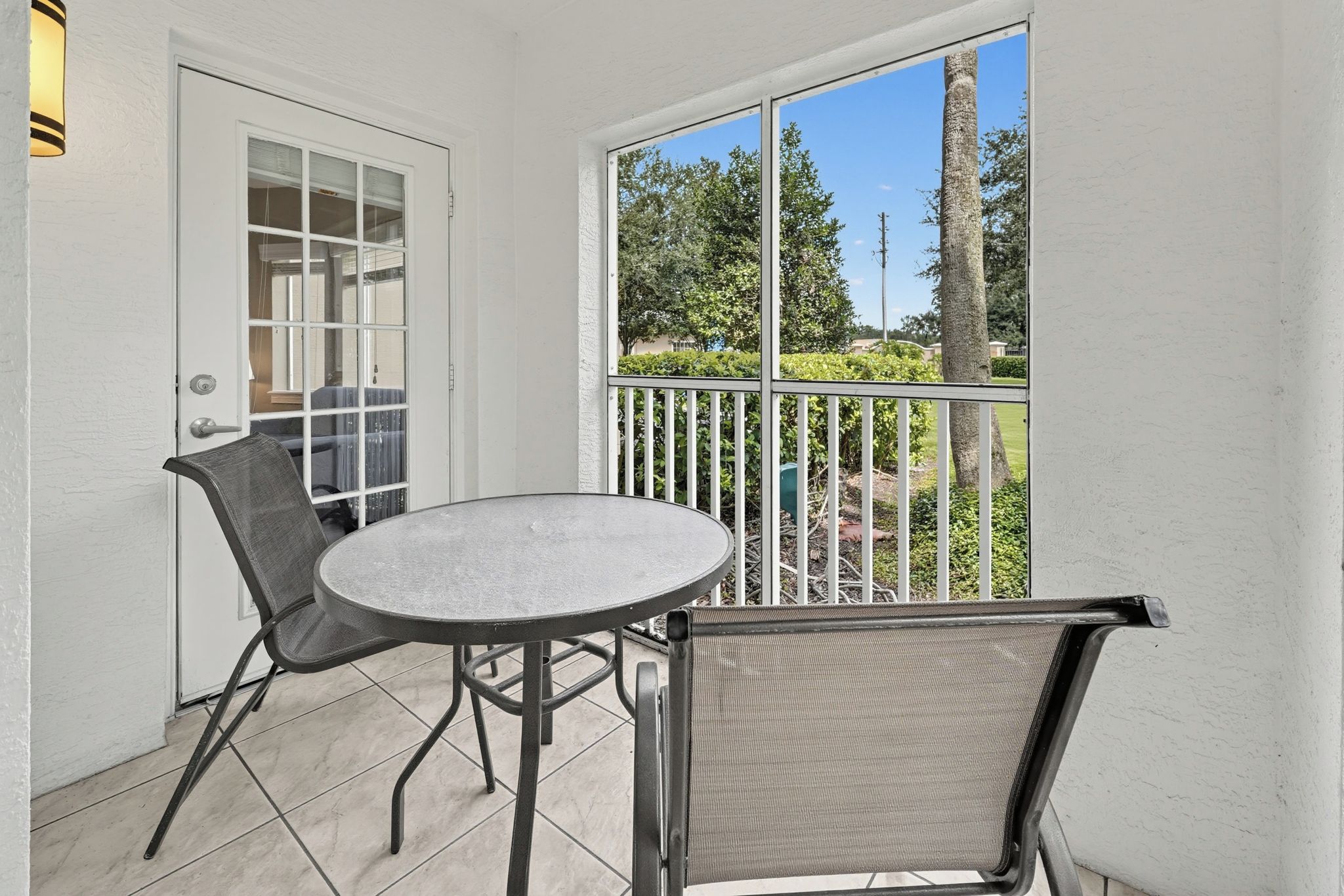 A small outdoor patio with a round table and two chairs, a door, and a view of a residential area.