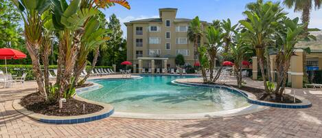 A pool area with lounge chairs and palm trees, surrounded by a building with multiple balconies.