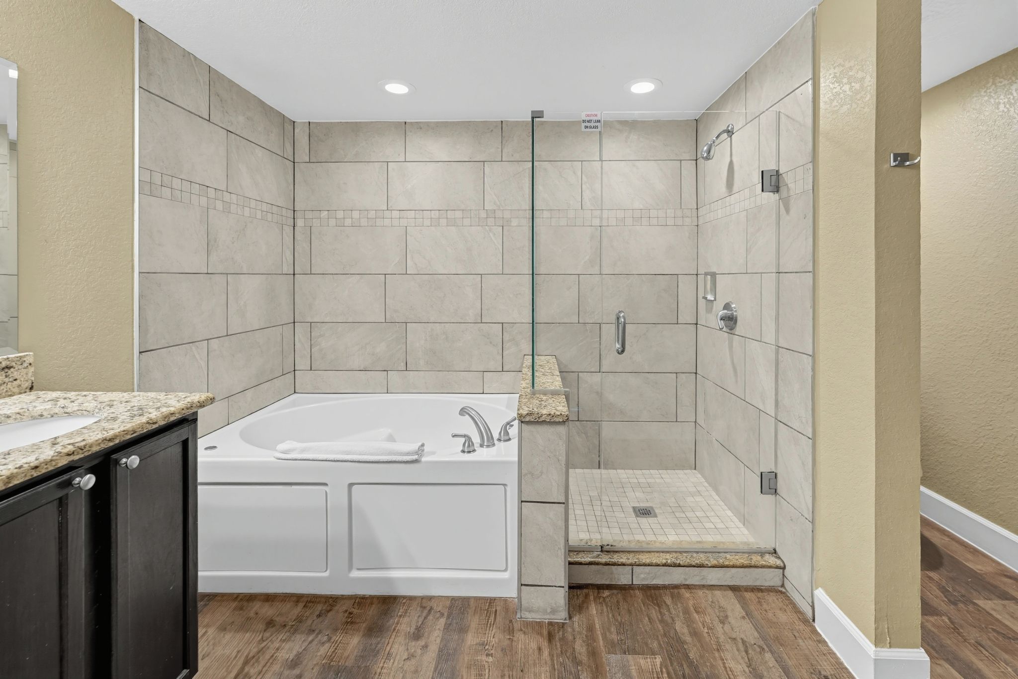 A modern bathroom with a freestanding bathtub, a glass-enclosed shower, and a wooden floor.