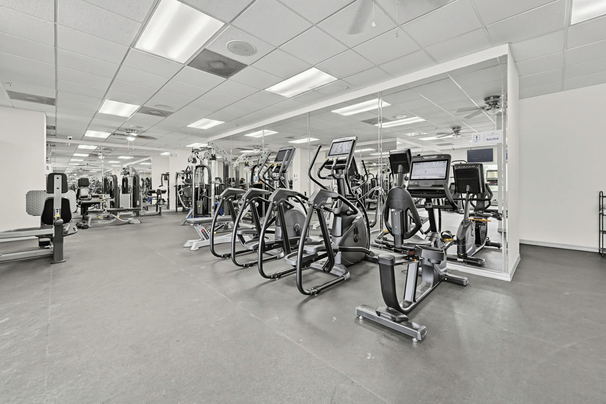 Een fitnessruimte met diverse trainingsapparaten, spiegels en een sauna.