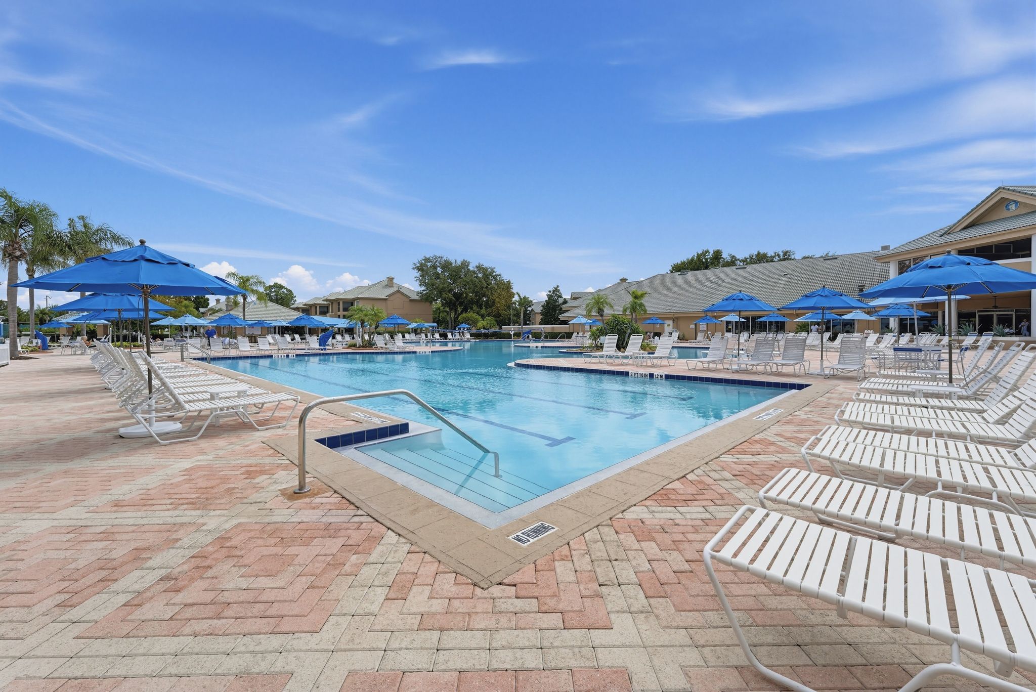 A pool area with multiple lounge chairs and umbrellas, surrounded by a brick patio.