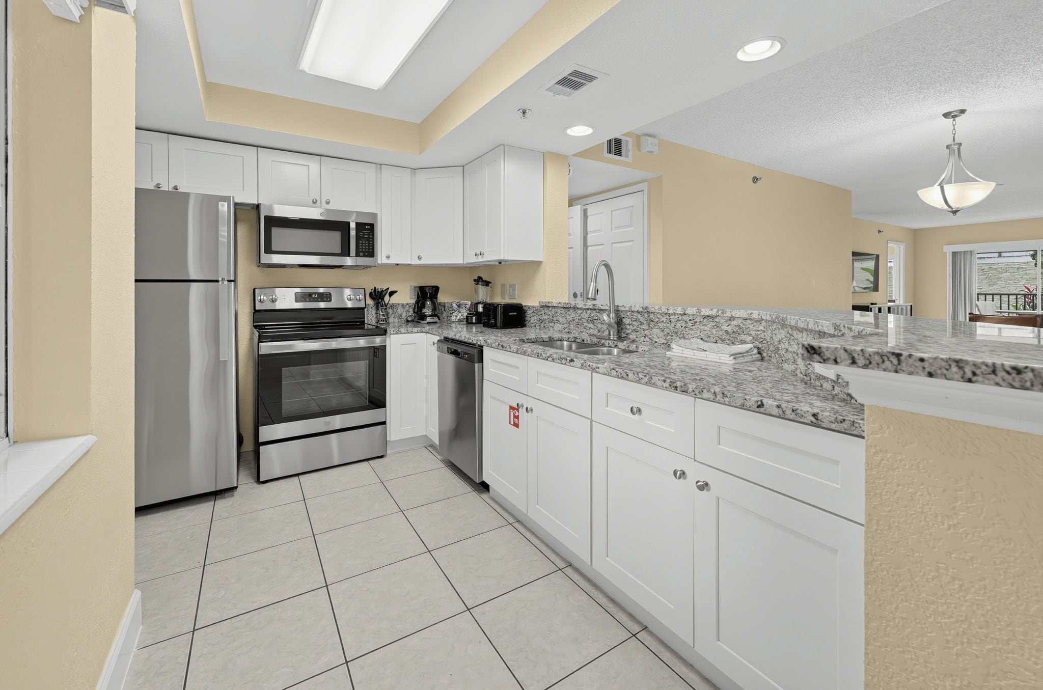 A modern kitchen with stainless steel appliances, white cabinetry, and a tiled floor.