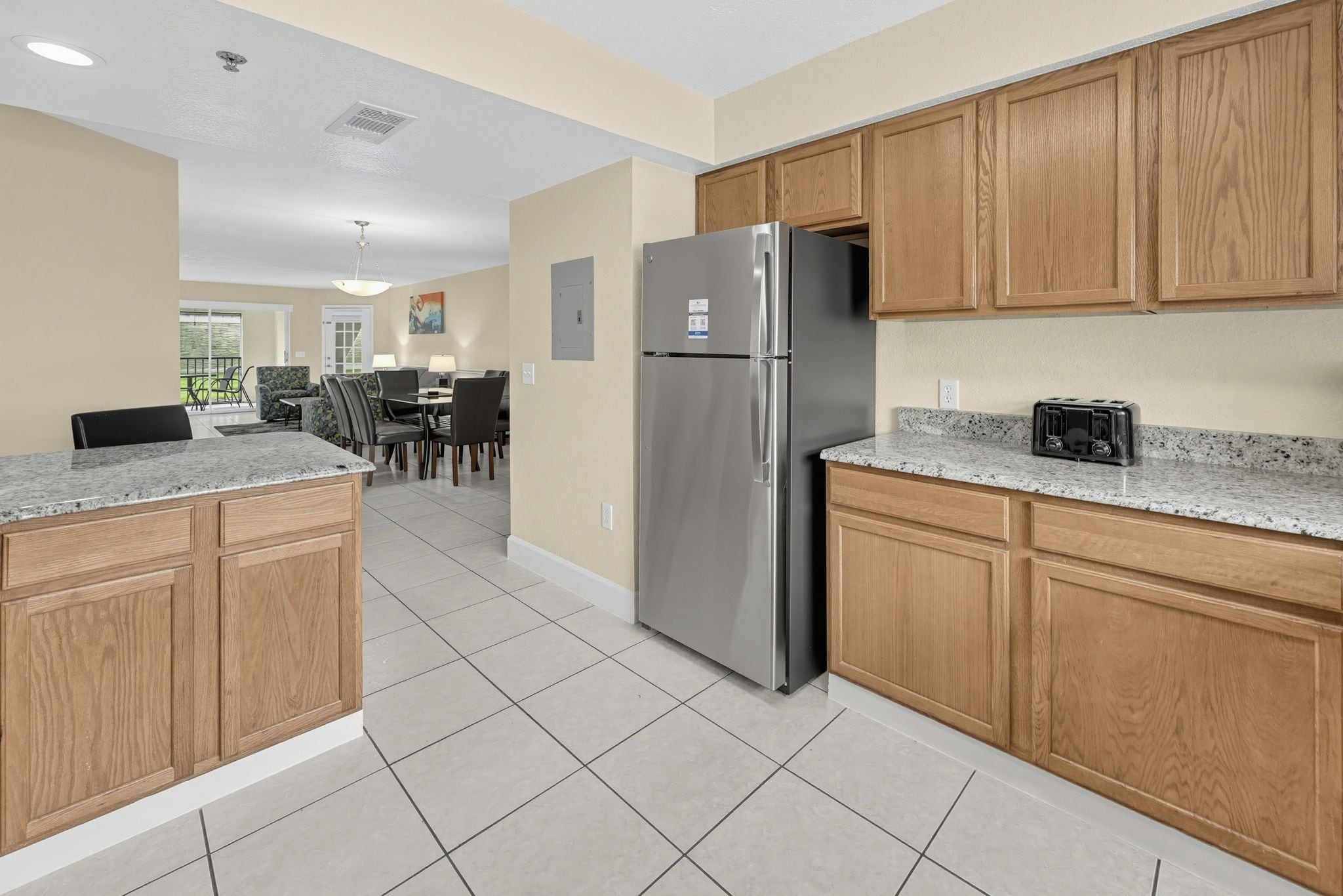 A modern kitchen with wooden cabinets, a stainless steel refrigerator, and a granite countertop.
