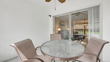 A glass-top round table with four chairs, a ceiling fan, and a sliding glass door leading to an outdoor area.