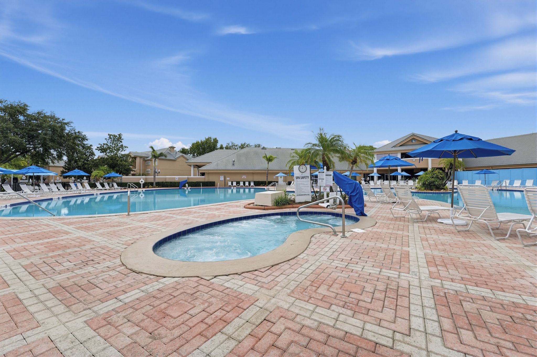 A pool area with lounge chairs and umbrellas, a hot tub, and a spa safety sign.