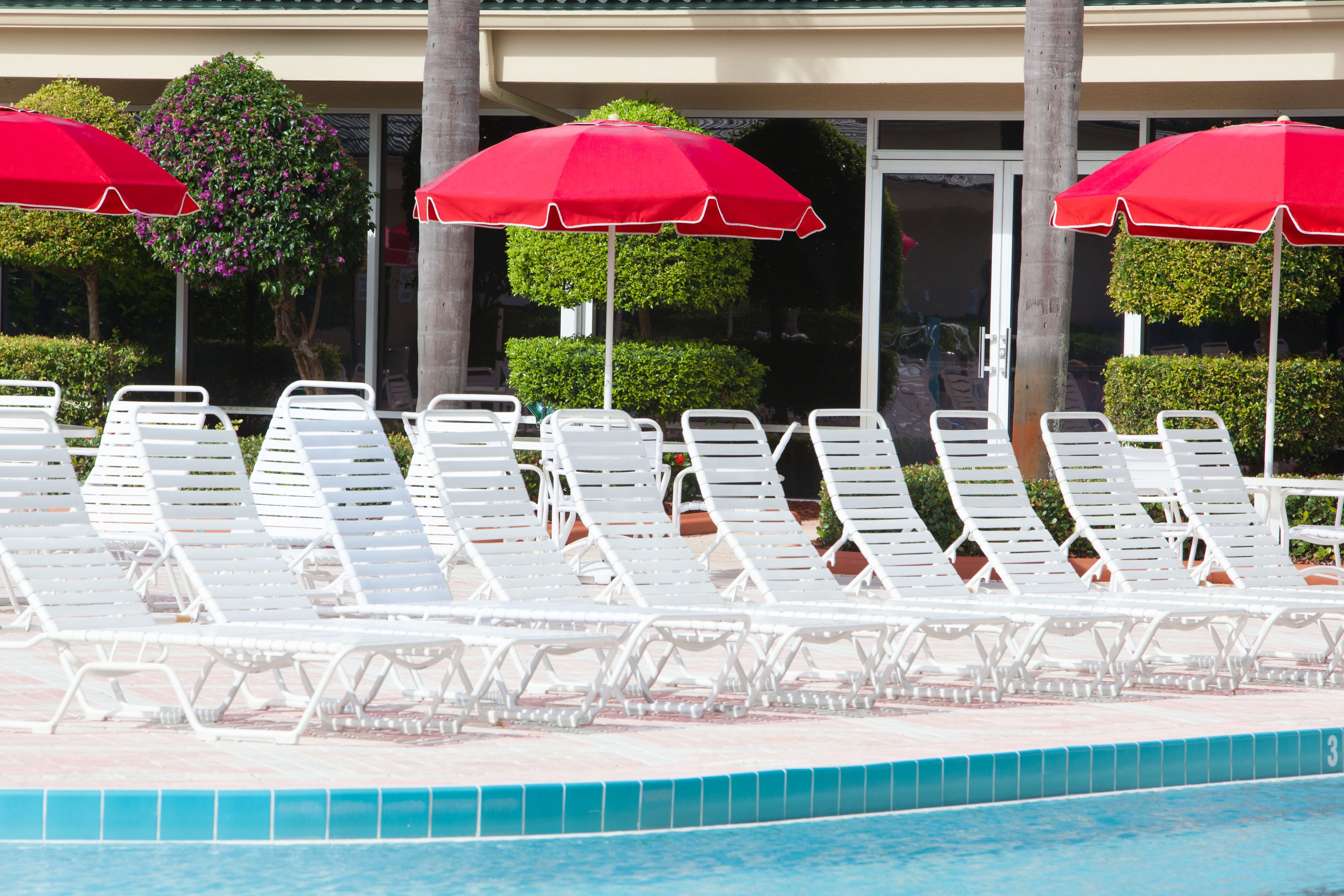 Zona de piscina con sillones blancos y sombrillas rojas.