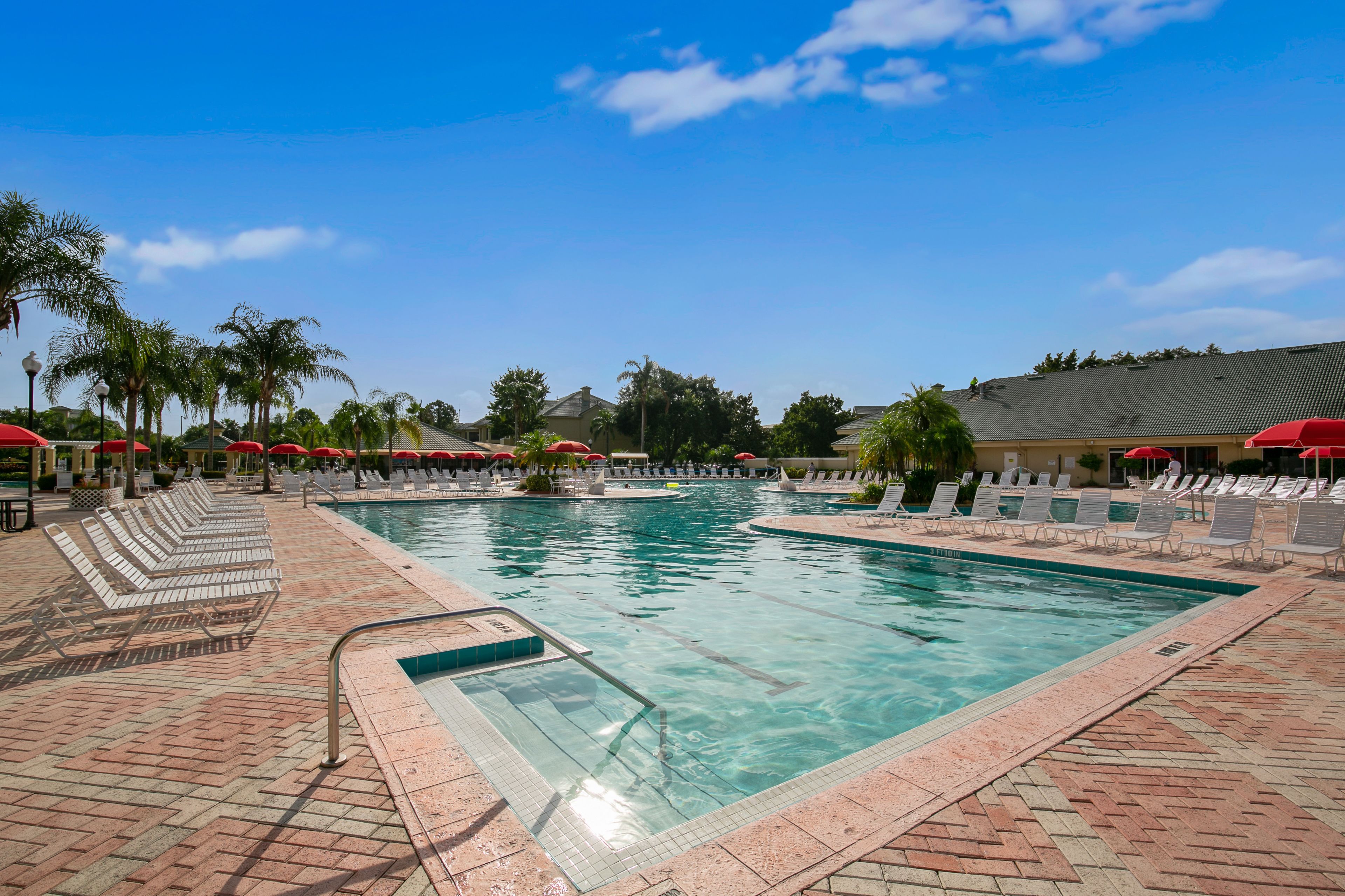 A swimming pool with lounge chairs and umbrellas, surrounded by palm trees and a clear sky.