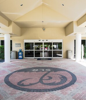 Entrada de hotel con puertas dobles, un logotipo circular en el suelo y un cartel.