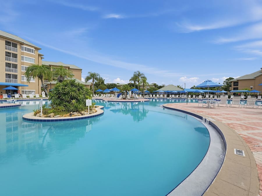 A swimming pool with lounge chairs and umbrellas, surrounded by a building with balconies.