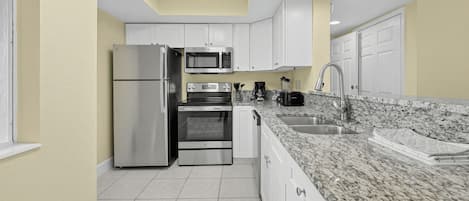 A modern kitchen with white cabinets, stainless steel appliances, a granite countertop, and a tiled floor.