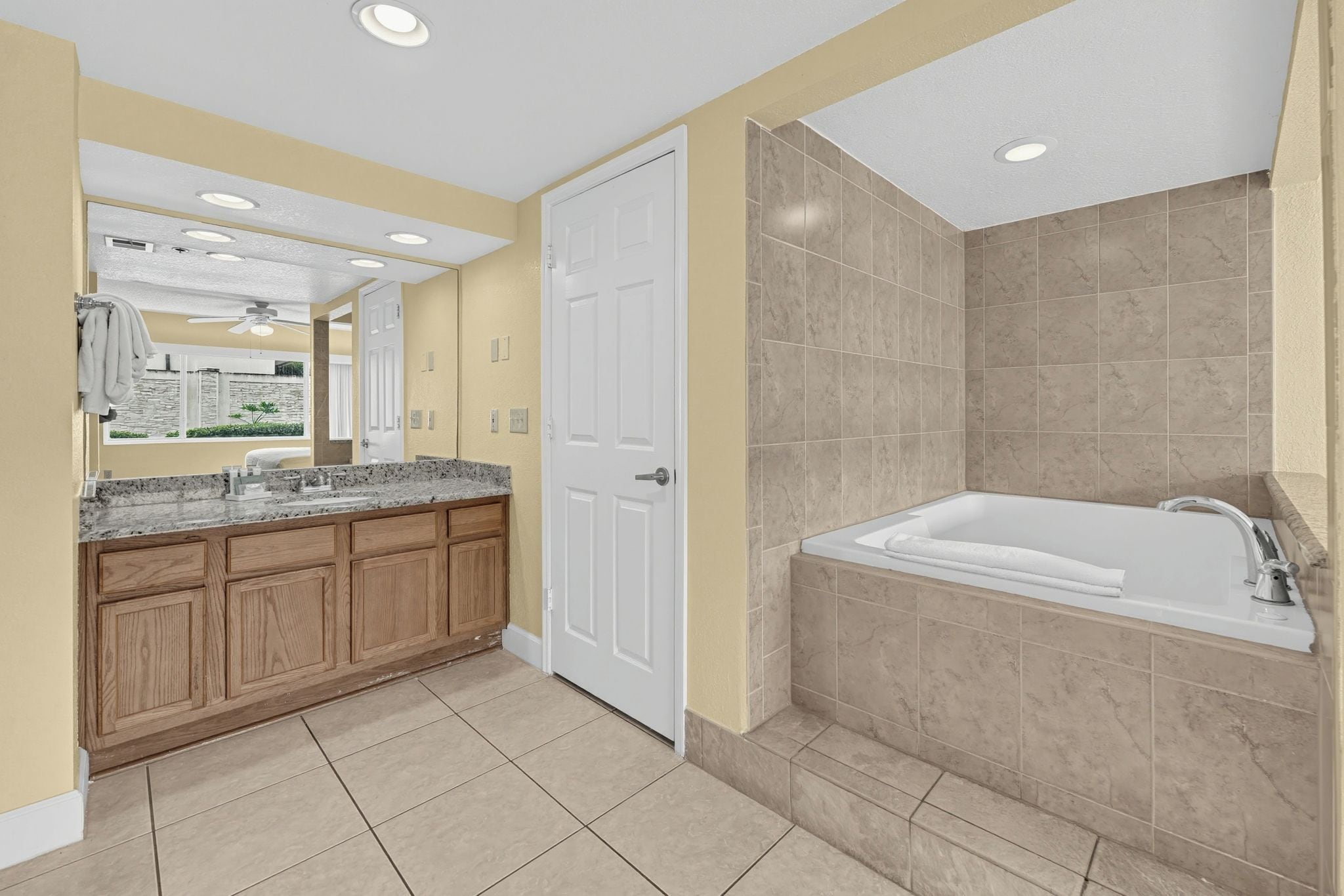 A bathroom with a large bathtub, a vanity with a granite countertop, and beige tiled walls.