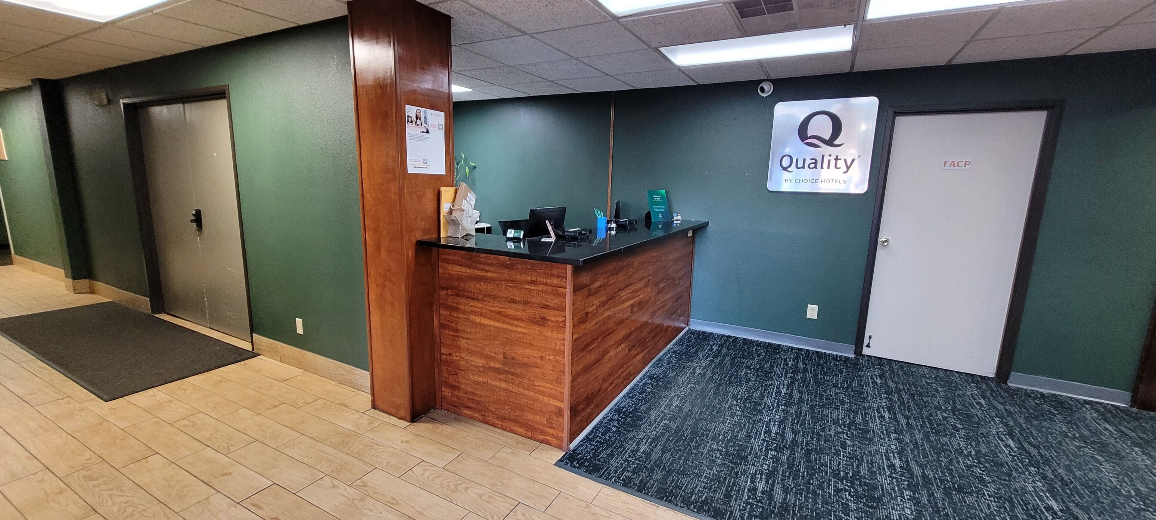 Un hall d’hôtel avec un comptoir d’accueil en bois, une enseigne indiquant « Qualité garantie par Choice Hotels » et une porte portant l’inscription « FACP ».