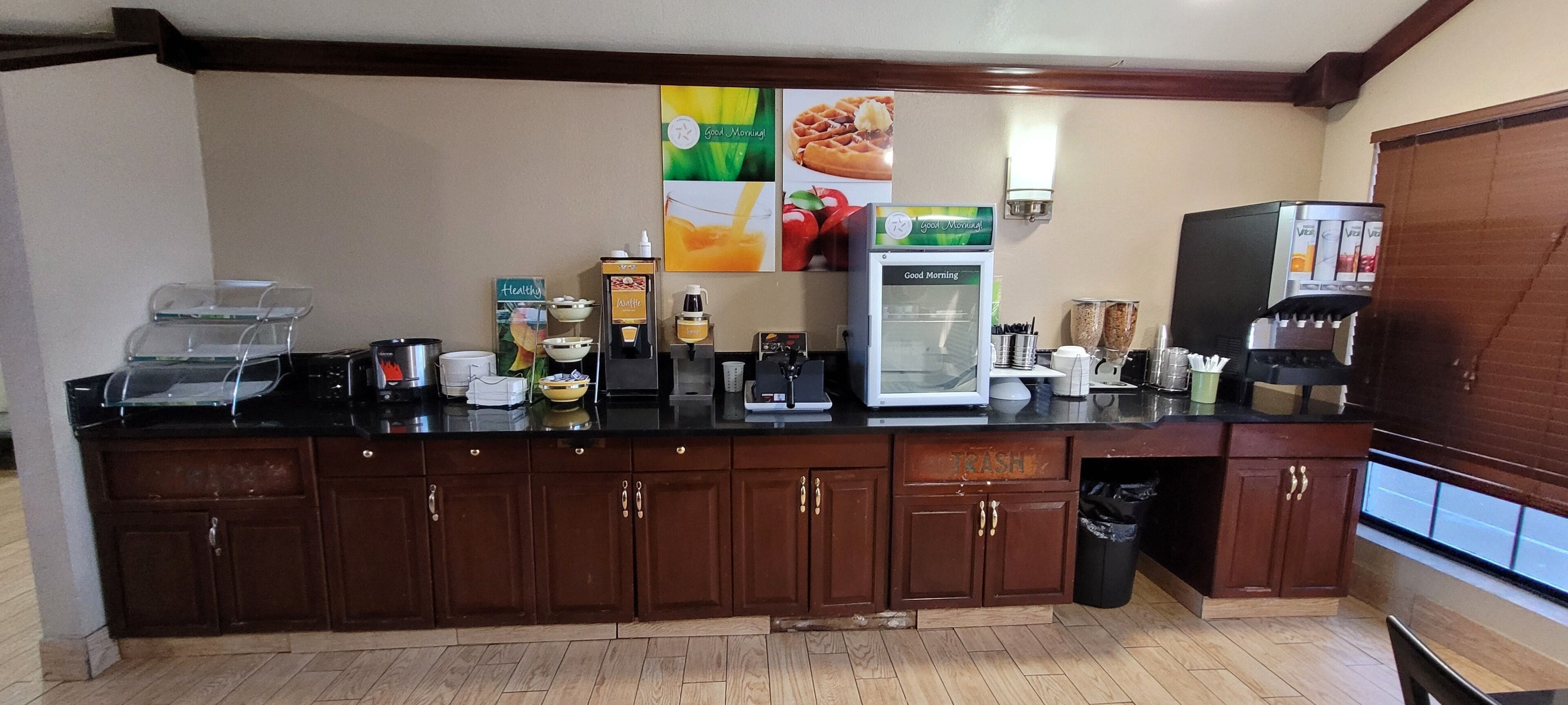A kitchen area with a coffee station, a refrigerator, and a trash bin.