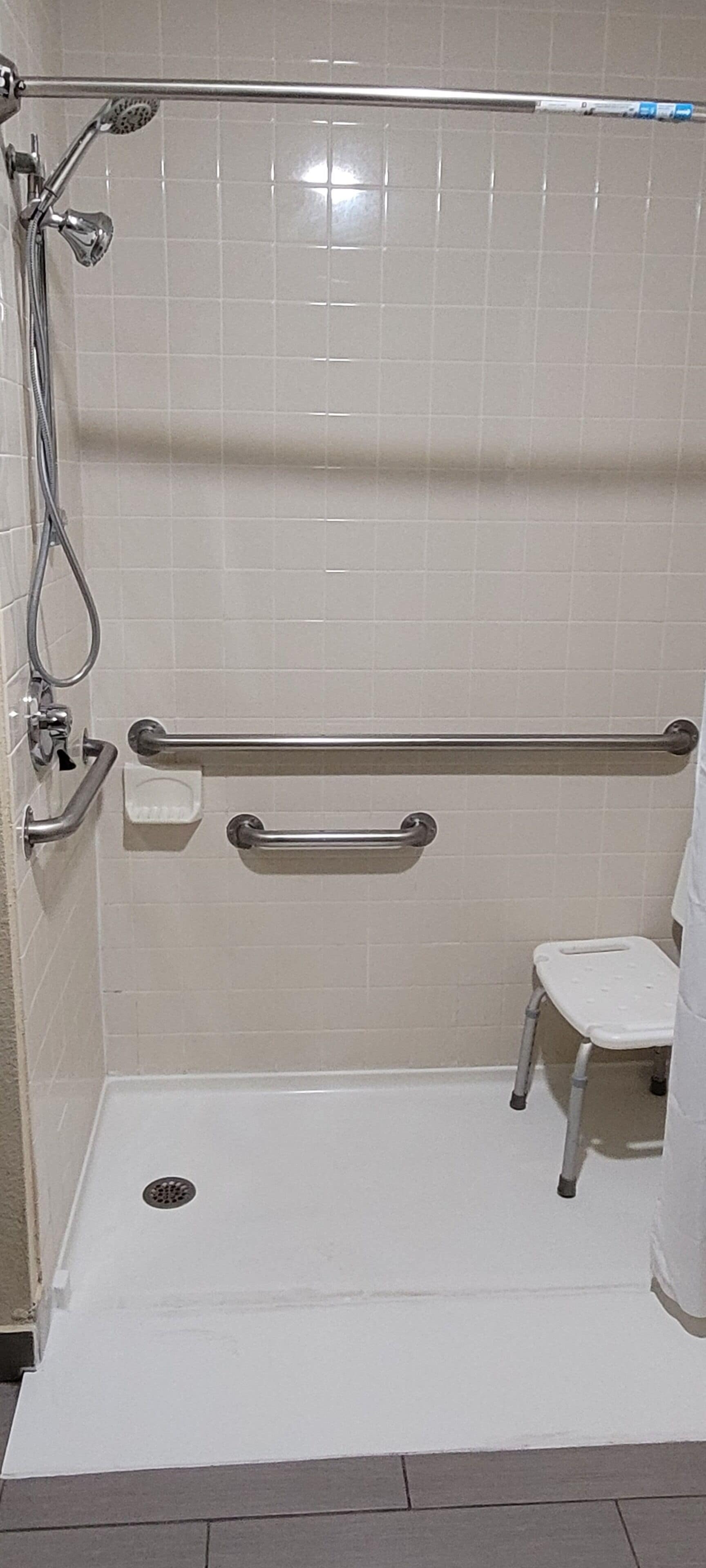 A bathroom with a walk-in shower, grab bars, a white toilet, and a small step stool.