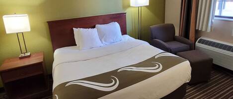 A hotel room with a large bed, two bedside lamps, a chair, and a heater.