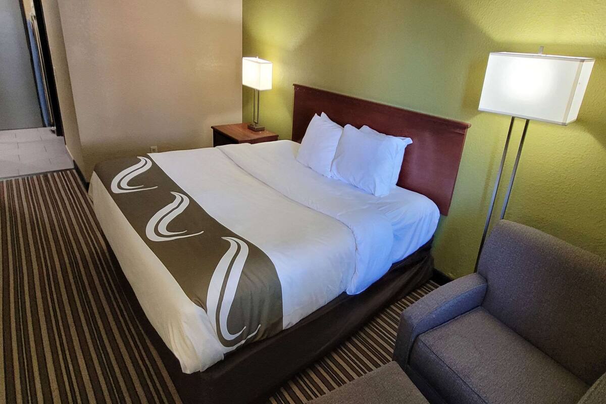 Ein Hotelzimmer mit einem Bett, einem Nachttisch, einem Sessel und zwei Wandlampen.