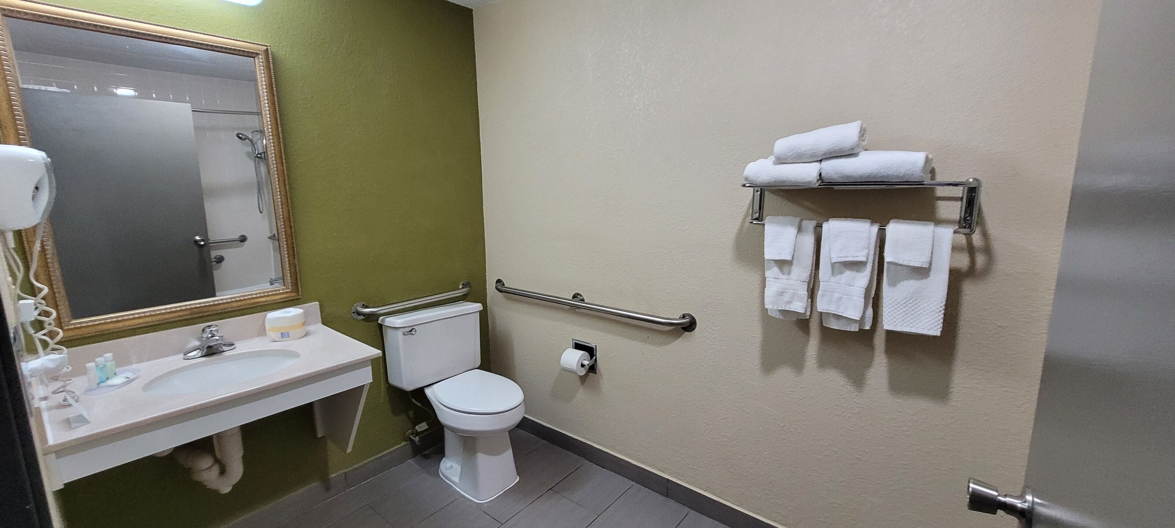 A bathroom with a sink, toilet, and hand dryer. There are towels on a rack.