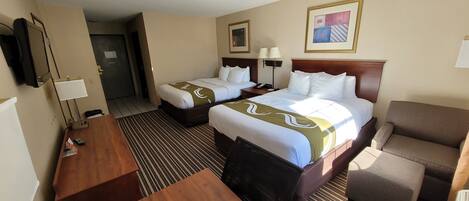 Een hotelkamer met twee bedden, een bureau, een stoel, een televisie en kunstwerken aan de muren.