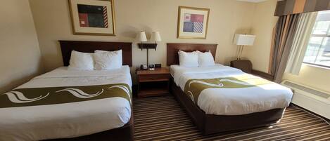 A hotel room with two beds, a nightstand, a lamp, and two framed pictures on the wall.