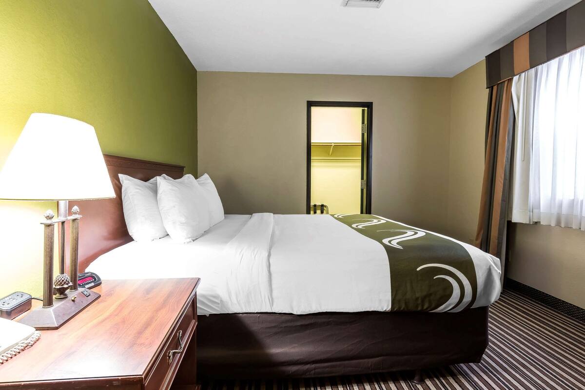 Ein Hotelzimmer mit Bett, Nachttisch, Lampe und Blick auf den Flur.