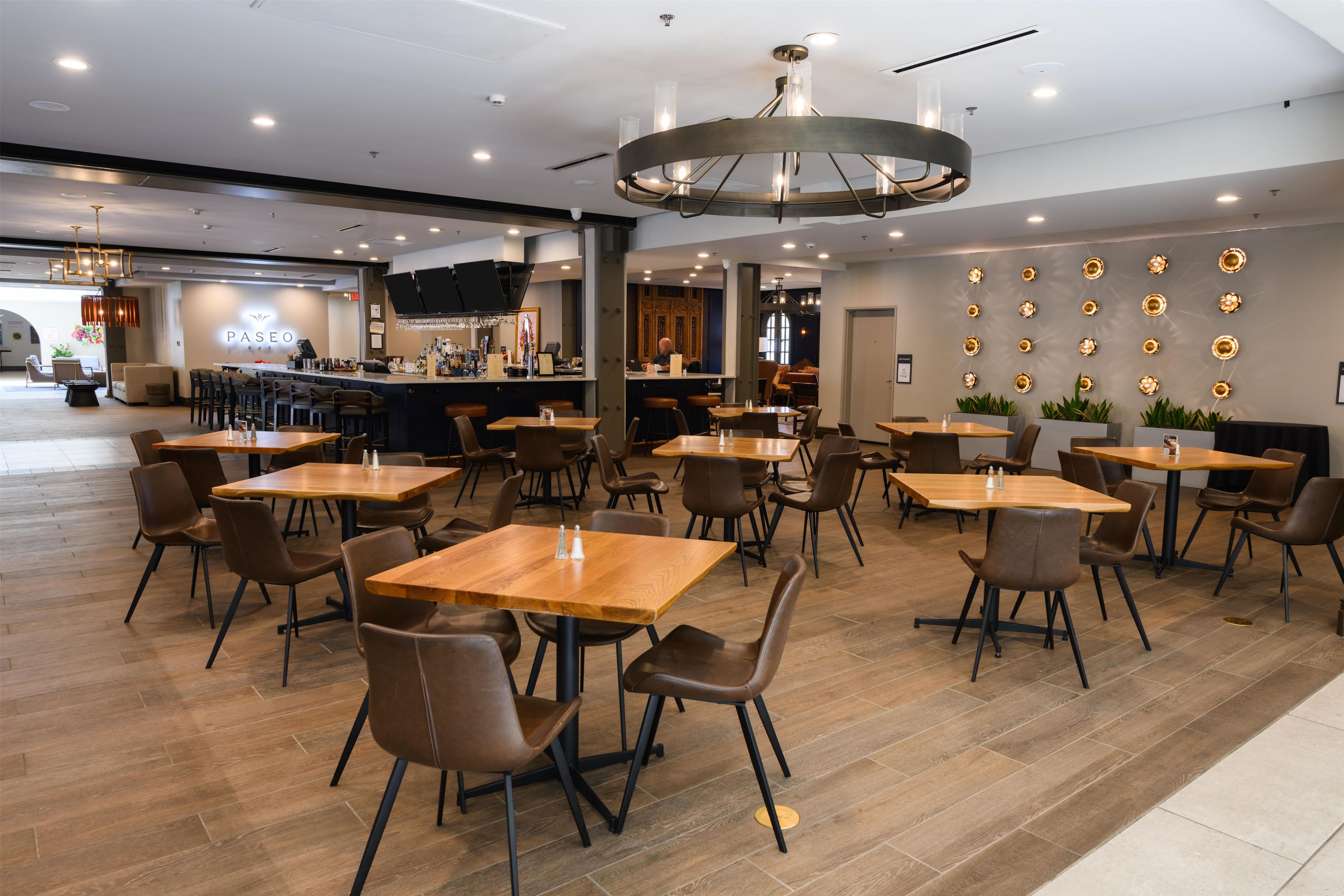 A modern restaurant with wooden tables and chairs, a bar area, and a wall decorated with circular light fixtures.