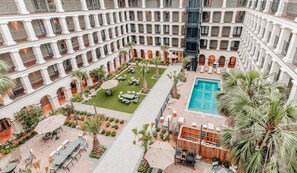 Un vestíbulo de hotel de varios niveles con un patio central, asientos al aire libre y una piscina.