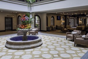Eine Lobby mit einem zentralen Brunnen, einer Sitzecke und einem Empfangsschalter.