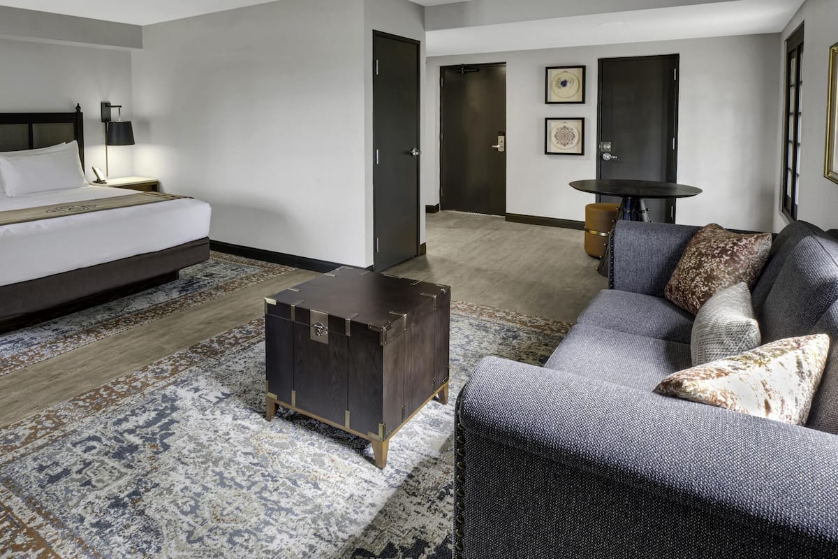 A hotel room with a bed, a sofa, a small table, a cabinet, and a door leading to another room.