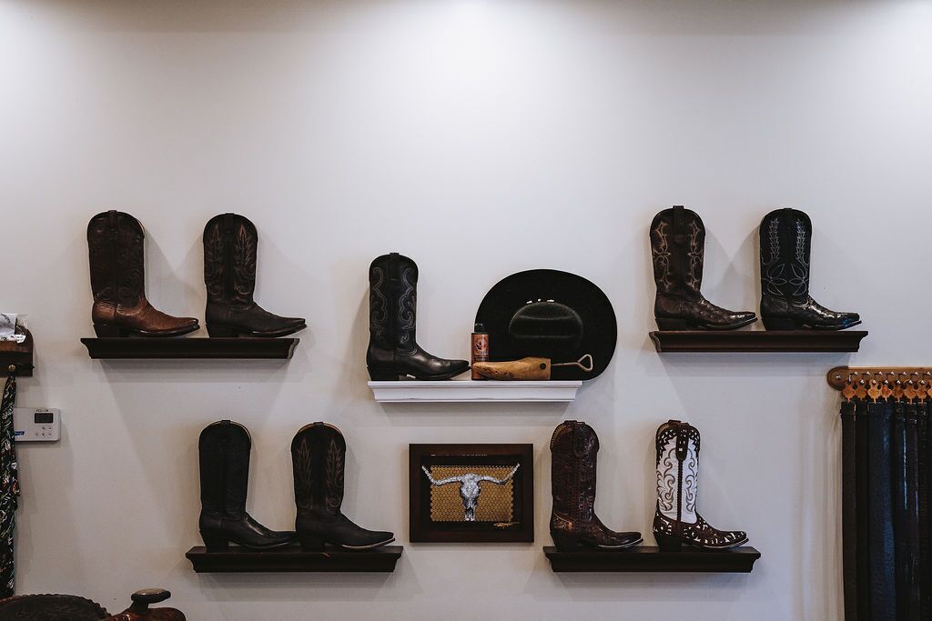 Diverse cowboylaarzen staan op planken voor een witte muur.