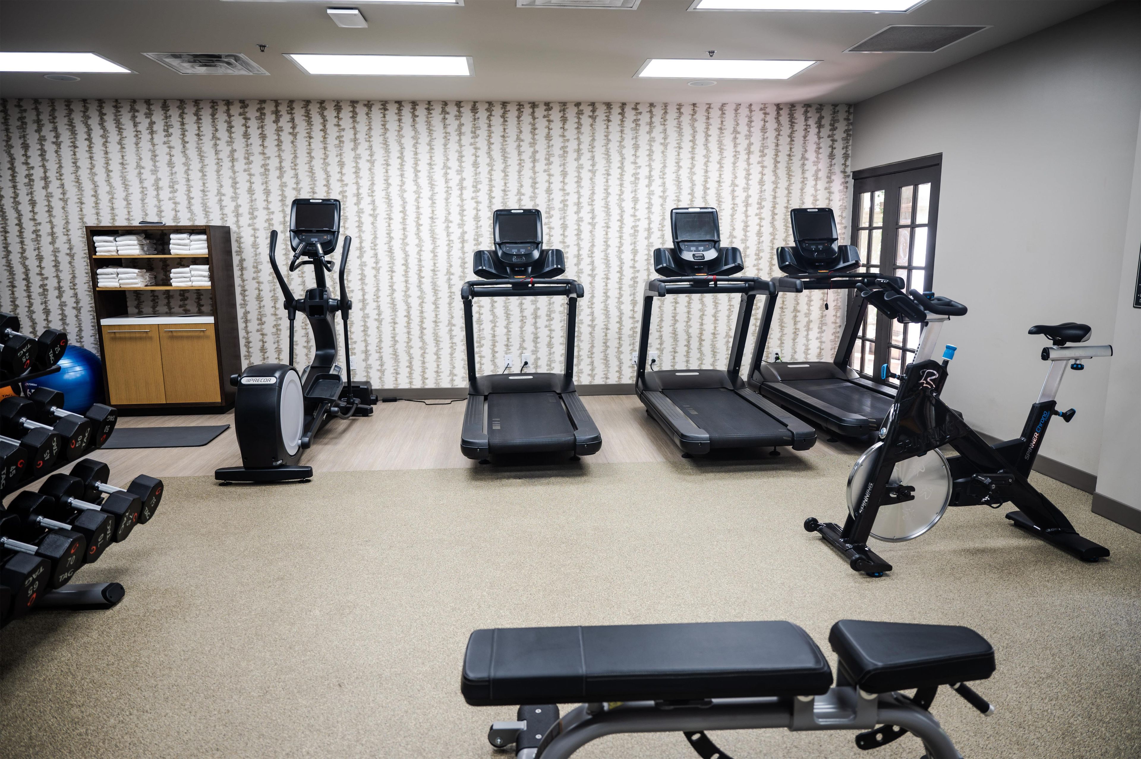 A gym with treadmills, an elliptical, dumbbells, and a bench.